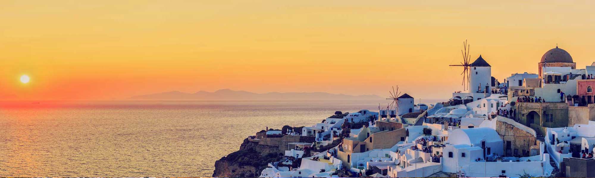 Santorini sunset with white-washed buildings, windmills, and pink dome church overlooking calm sea