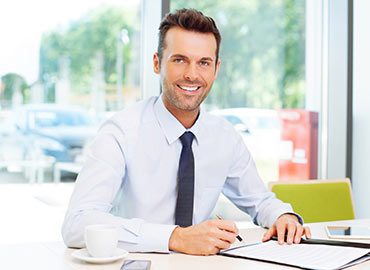 Professional man in white shirt and tie smiling at desk with laptop