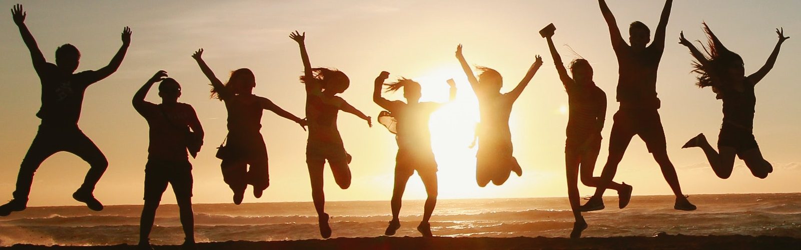Group of people jumping and dancing on beach at sunset with raised arms
