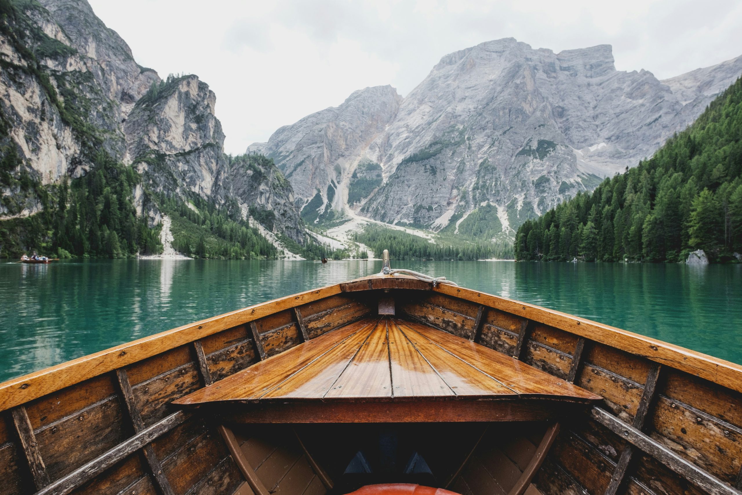 Wooden boat bow on turquoise alpine lake surrounded by steep rocky mountains and pine forests
