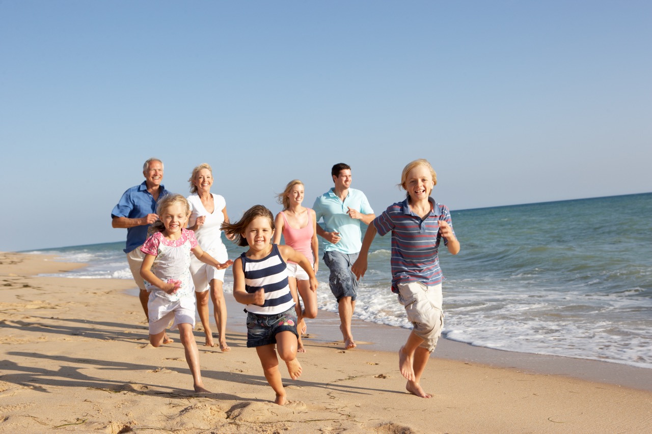 Multi-generational family running together on sandy beach with ocean waves in background