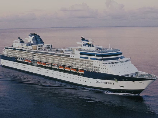 Large white cruise ship with blue accents sailing on calm ocean water