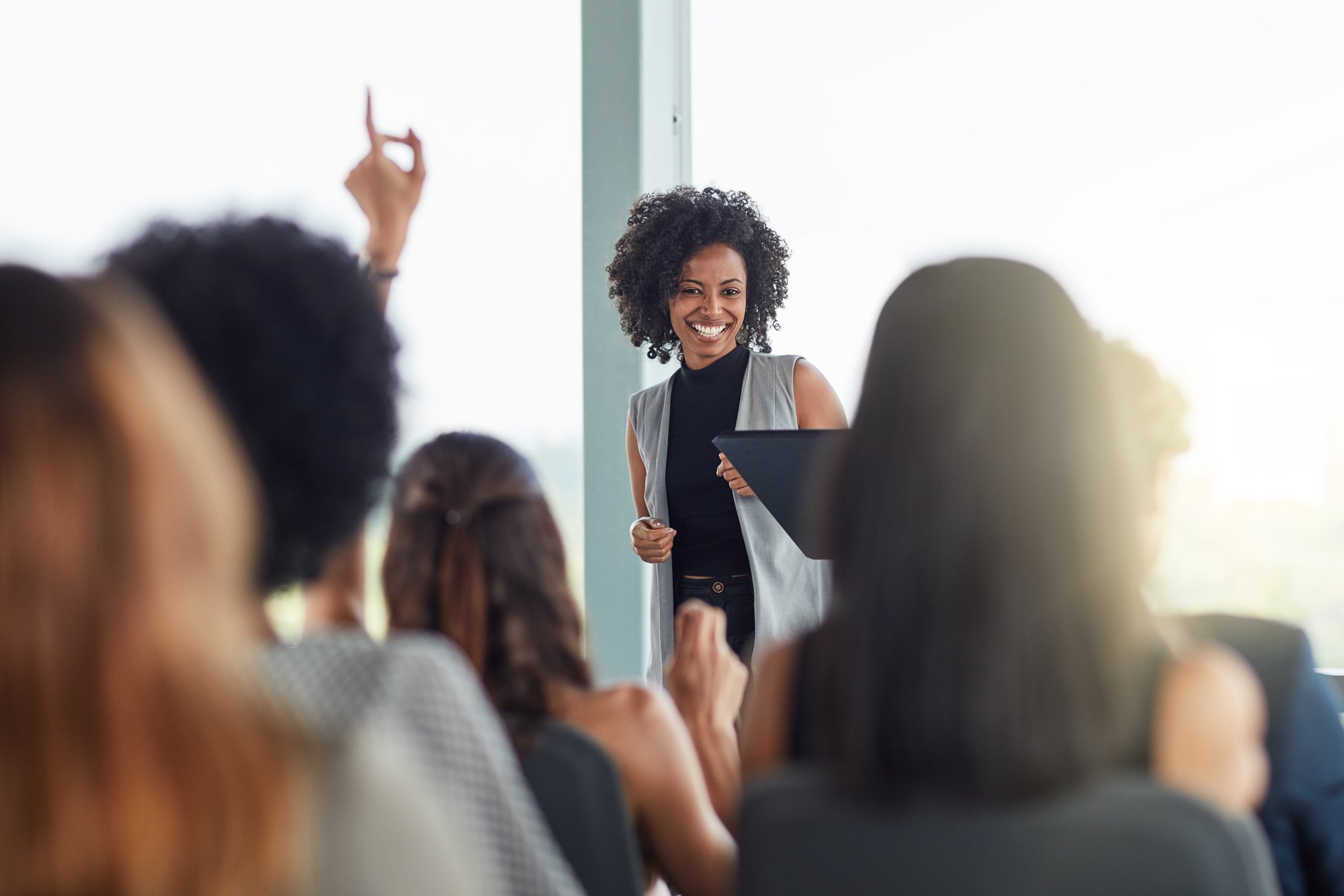 Professional Training Session with Engaged Audience A confident female presenter with curly hair smiles while addressing an audience during a training